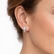 Close-up of an ear wearing a silver cross earring on a white background