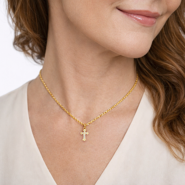 Gold necklace with a cross pendant worn by a person on a white background