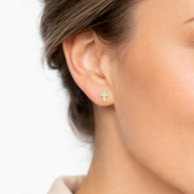 Close-up of an ear wearing a gold cross earring with a blurred background
